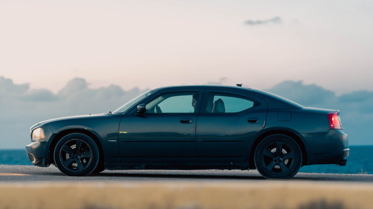 A sleek car parked by a coastal road in Libya during dawn, creating a serene scene.