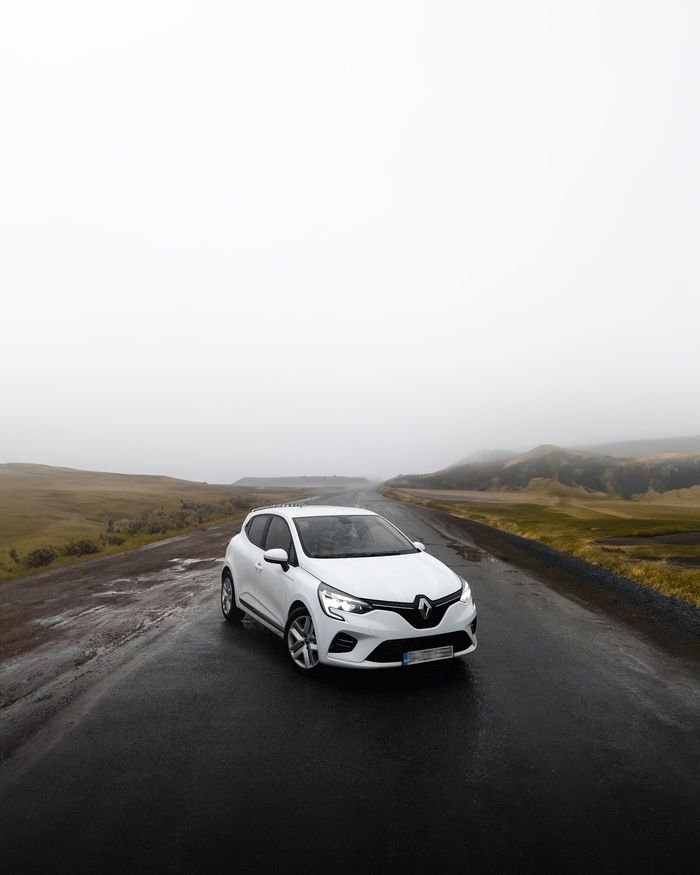 A sleek white Renault parked on a foggy road surrounded by mist-covered hills.
